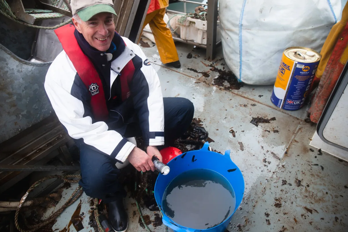 A crew member sampling the water with a scientific probe on deck