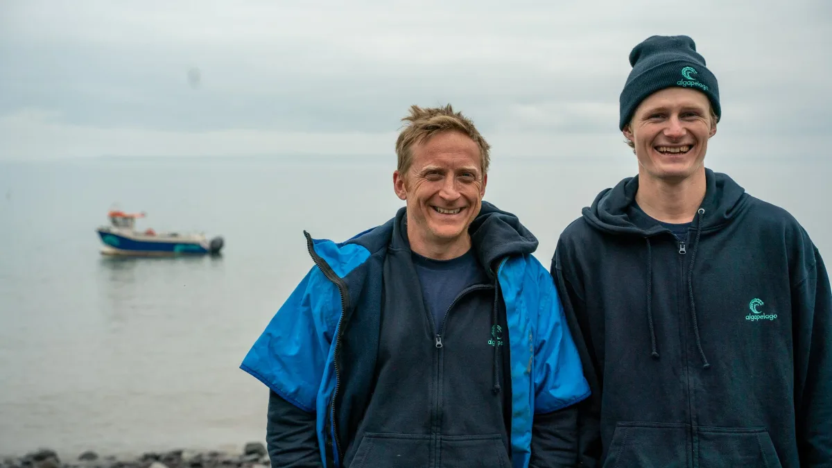 Two Algapelago crew on the beach, their workboat moored behind
