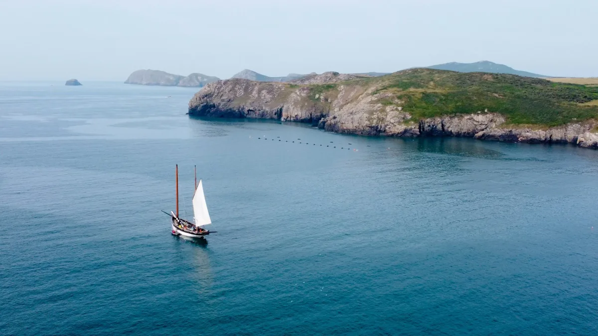 A gaff-rigged sailing boat on blue water beside the farm's float-line